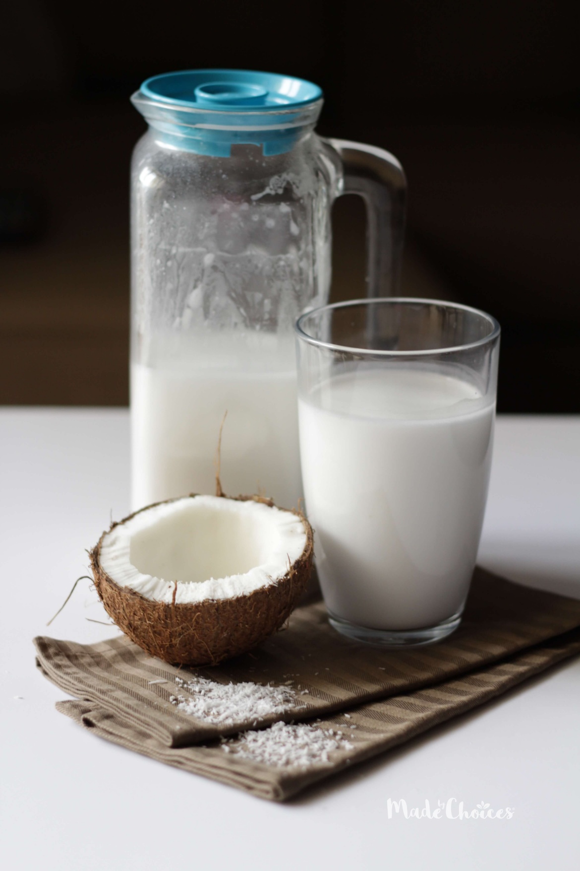 Frasco de leite de coco caseiro com copo de vidro e metade de um coco