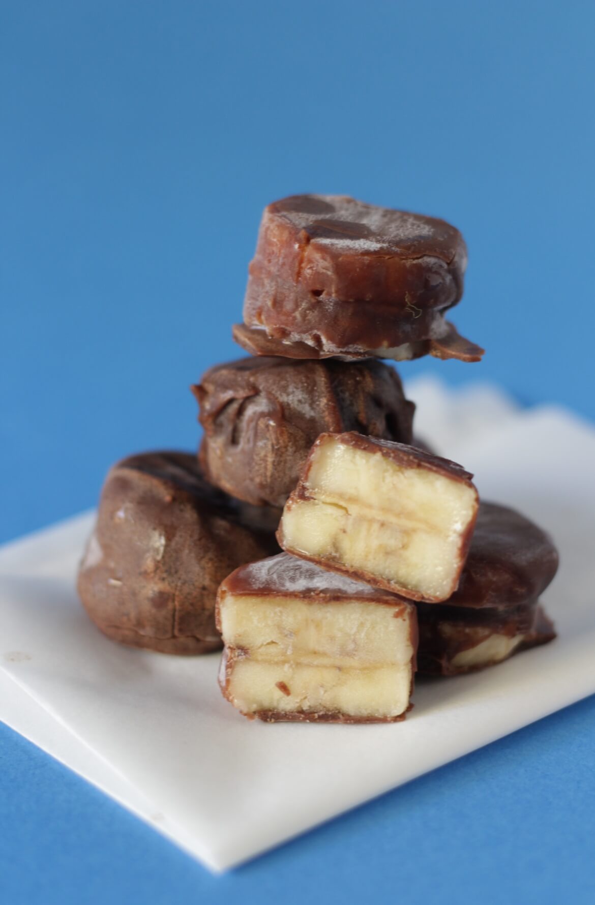 Vários mini gelados com duas rodelas de banana, manteiga de amendoim no meio e cobertos com chocolate. 