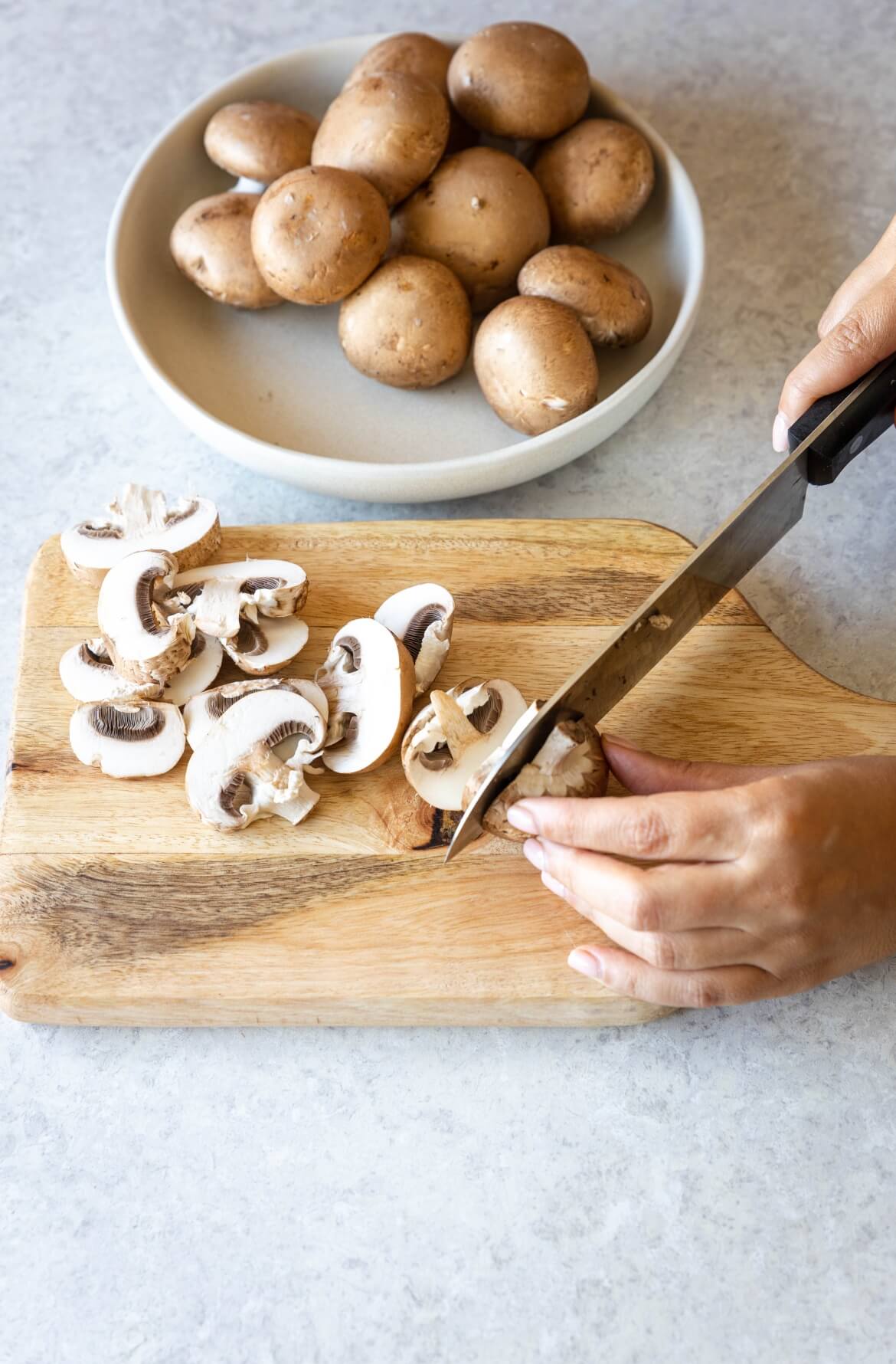uma tábua e uma mão a segurar uma faca a cortar cogumelos marron frescos
