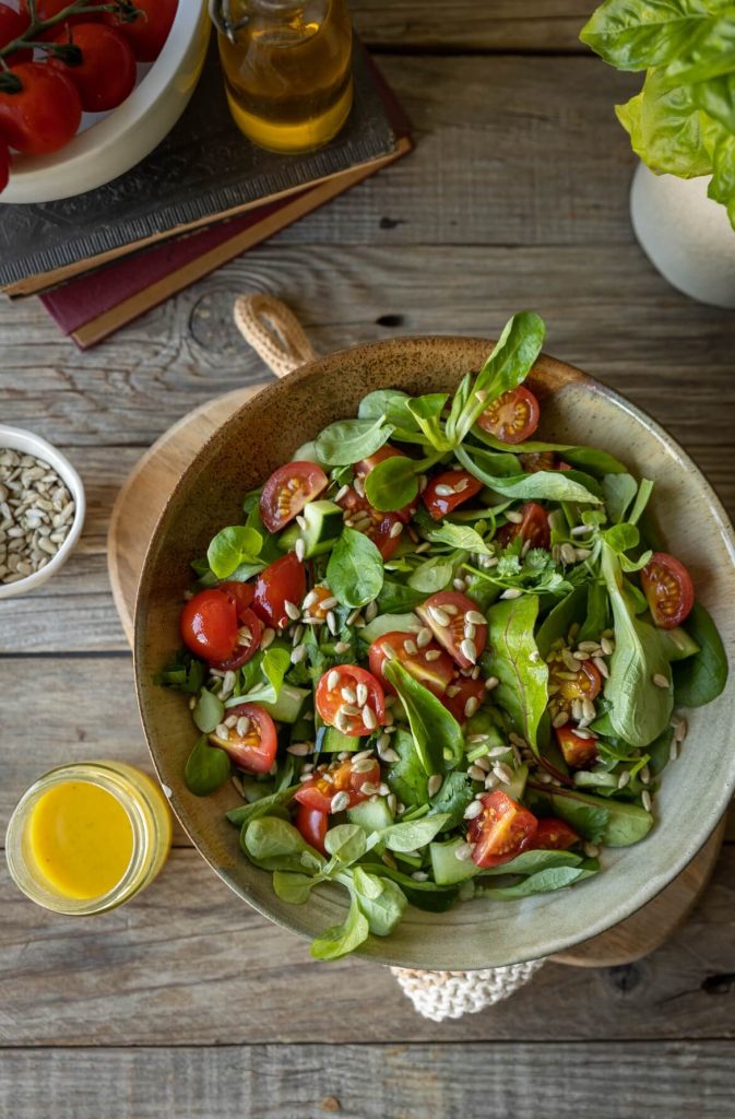 Salada de folhas verdes com canónigos, tomate cherry, pepino e sementes de girassol, servida numa taça rústica ideal como acompanhamento.