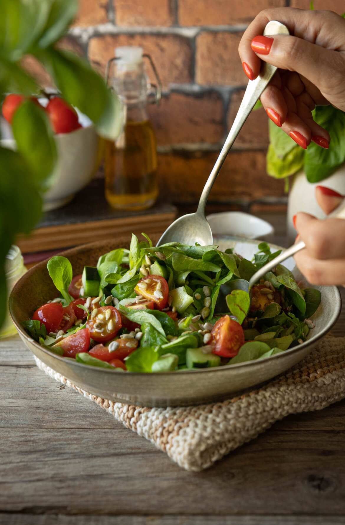 Salada de folhas verdes com canónigos, tomate cherry, pepino e sementes de girassol, servida numa taça rústica sobre um pano de malha, com mãos a servir – salada fresca, leve e saudável, ideal como acompanhamento.
