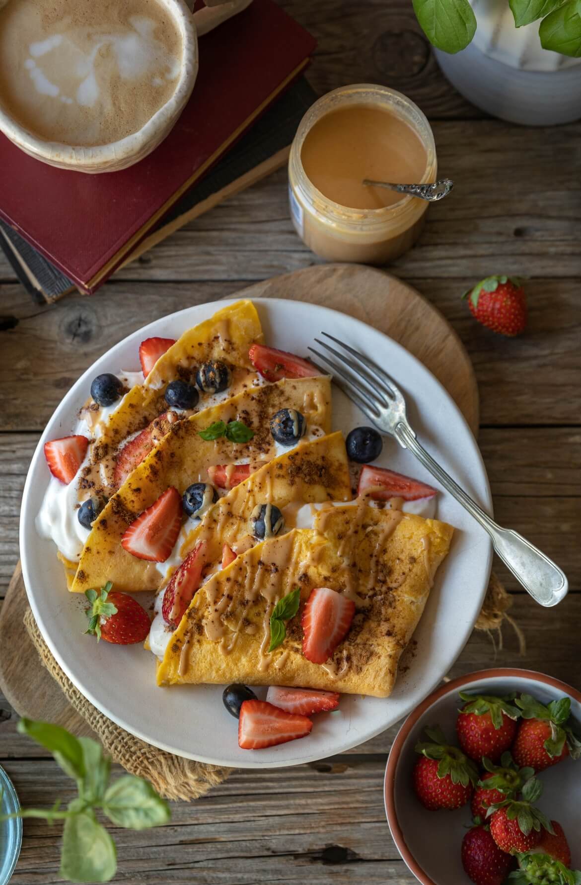 Crepioca doce simples com iogurte vegetal, morangos e mirtilos, servida com café e creme de amêndoa